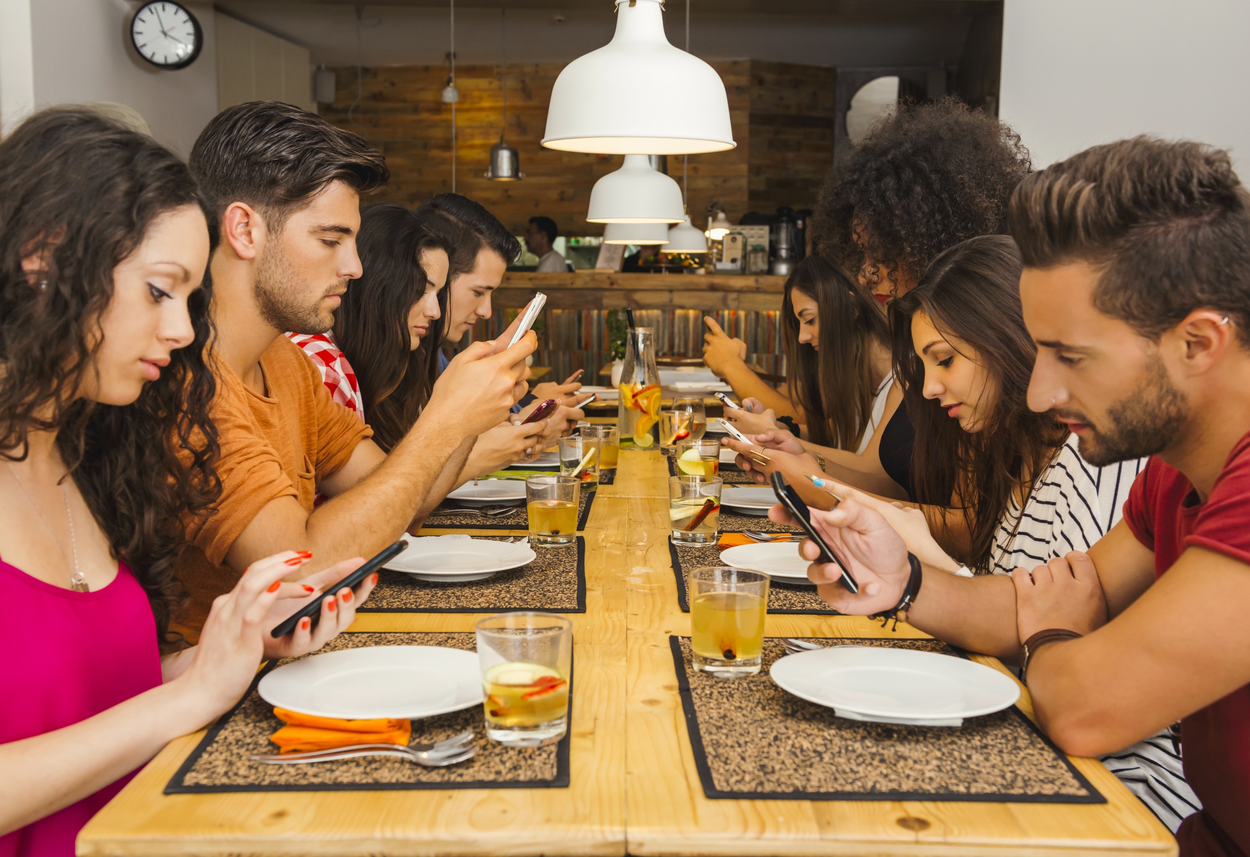 Group of friends at a restaurant with all people on the table occupied with Smartphones