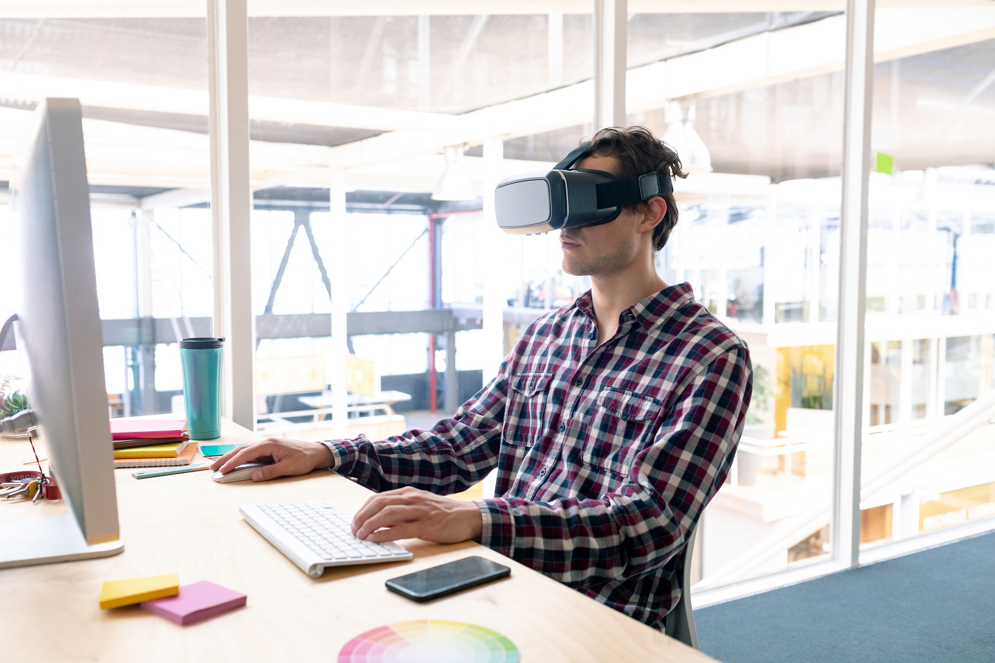 male employee using virtual reality headset while working on computer at a desk in the office