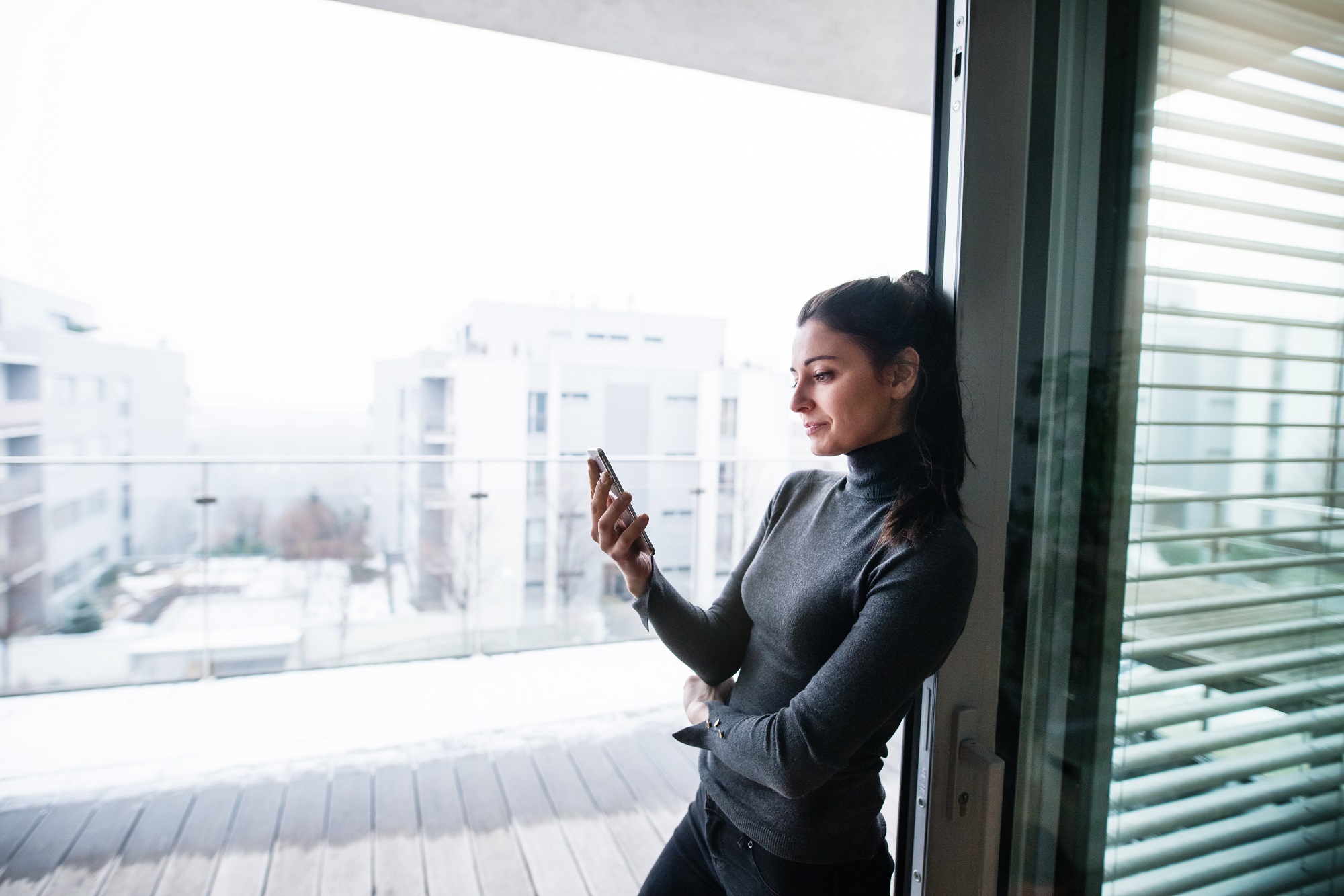 A woman standing by the window, holding smartphone.