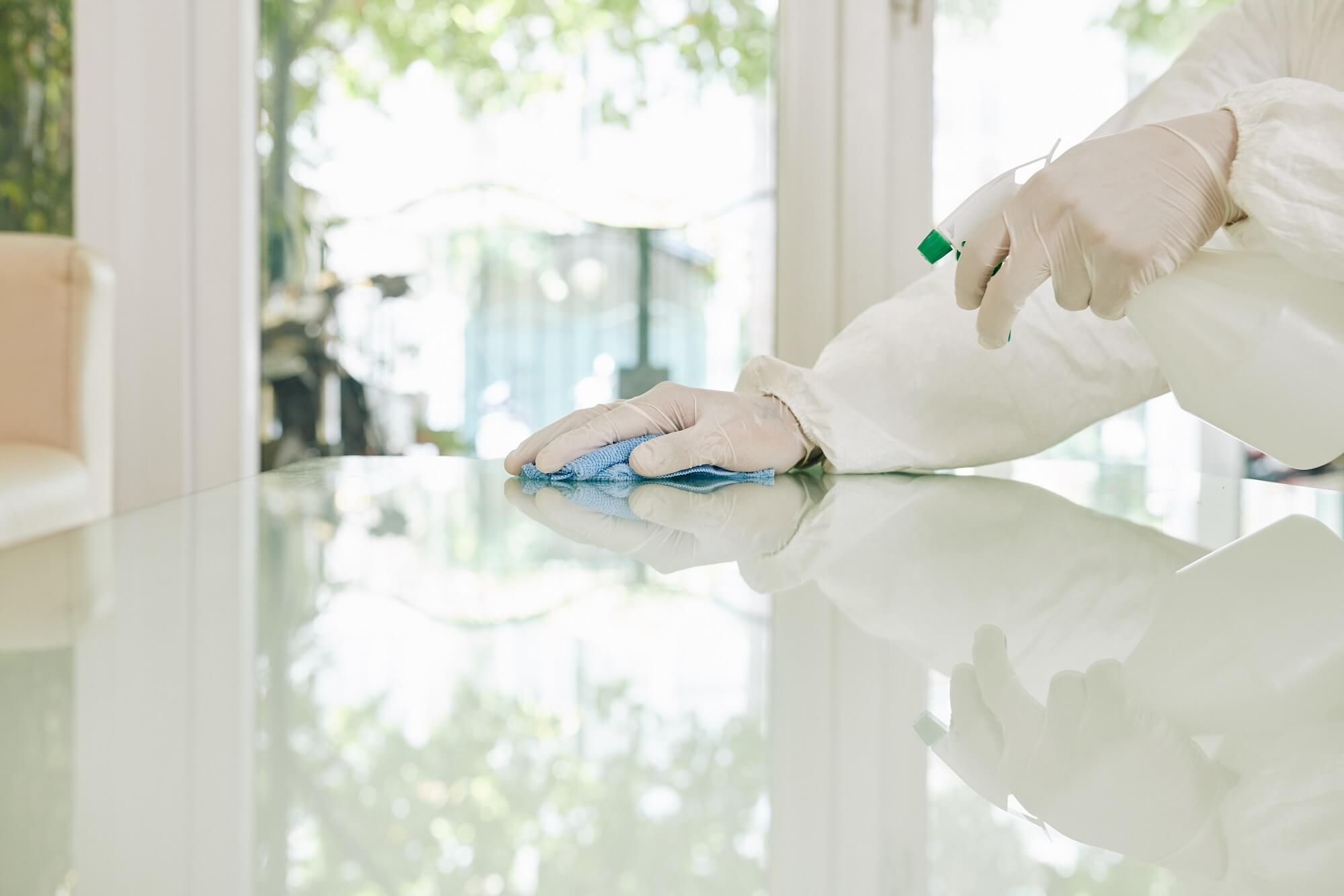 Worker in protective suit and rubber gloves wiping surfaces with special spray that kills viruses and bacteria