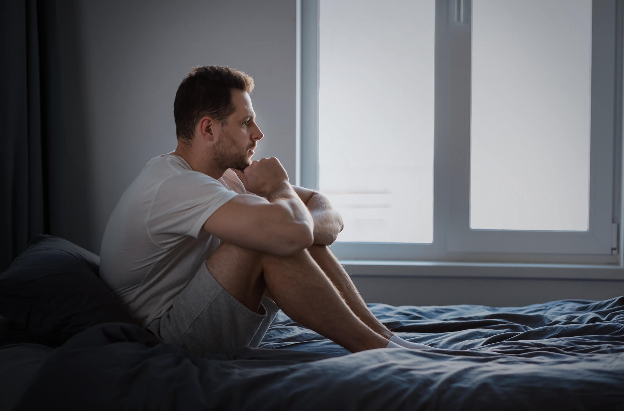 Depressed Man Thinking About Problems Sitting In Bed Indoors