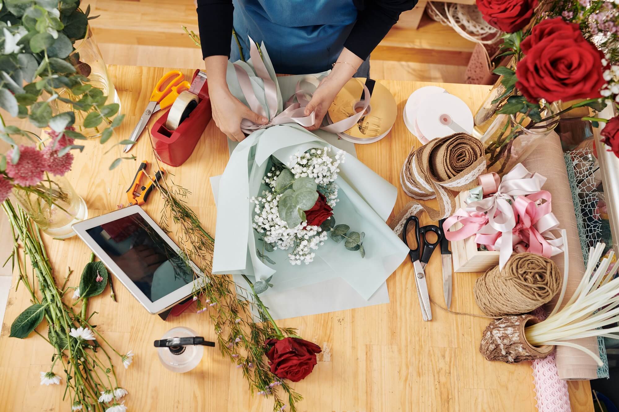 Hands of florist decorating bouquet of flowers with wrapping paper and ribbons