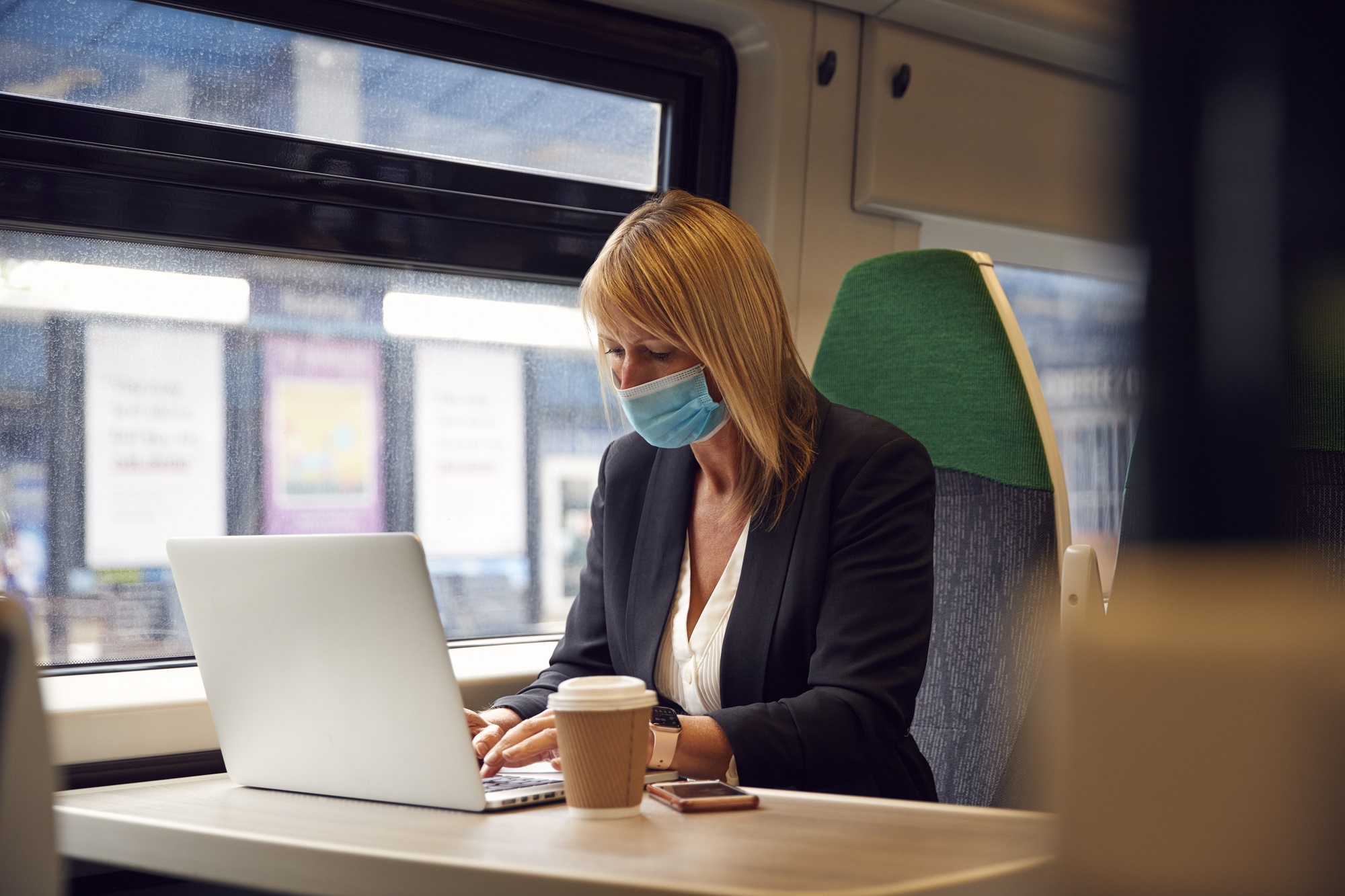Businesswoman On Train Working On Laptop Wearing PPE Face Mask During Health Pandemic