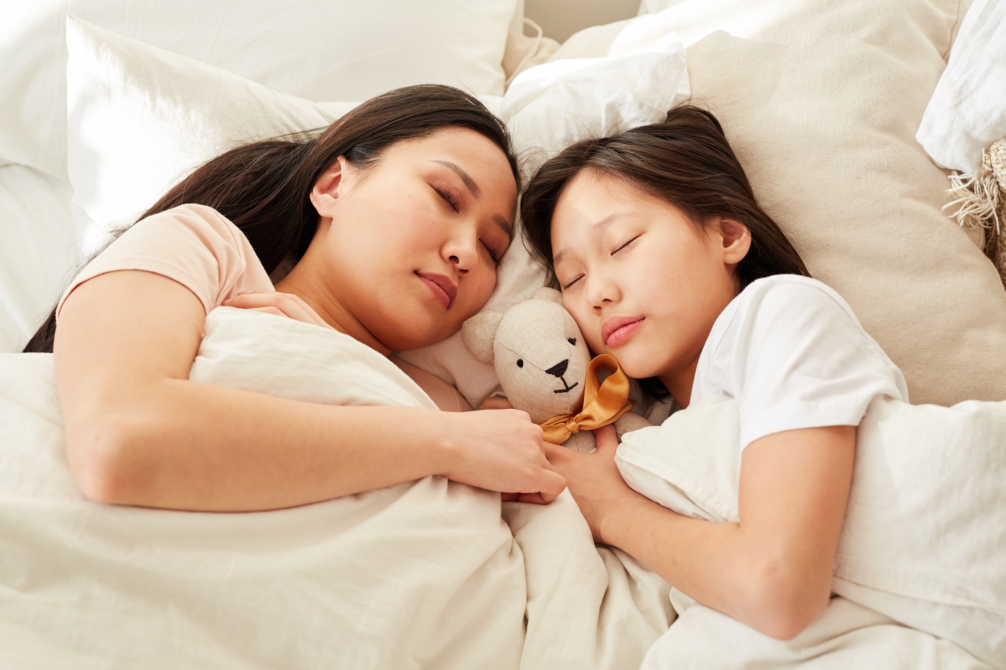 Asian mother sleeping together with her daughter in the bed in the bedroom