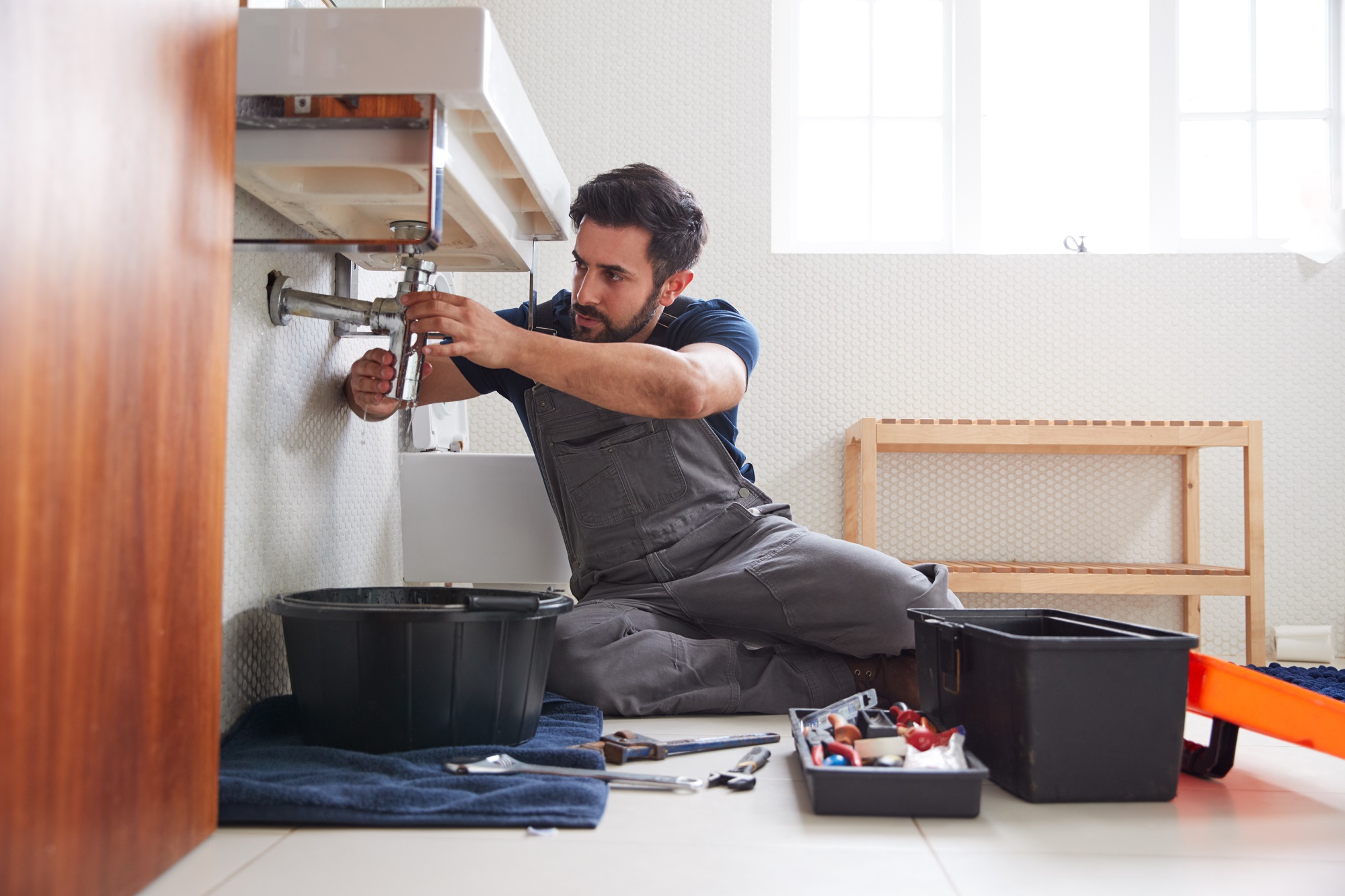  Plumber Working To Fix Leaking Sink In Home Bathroom