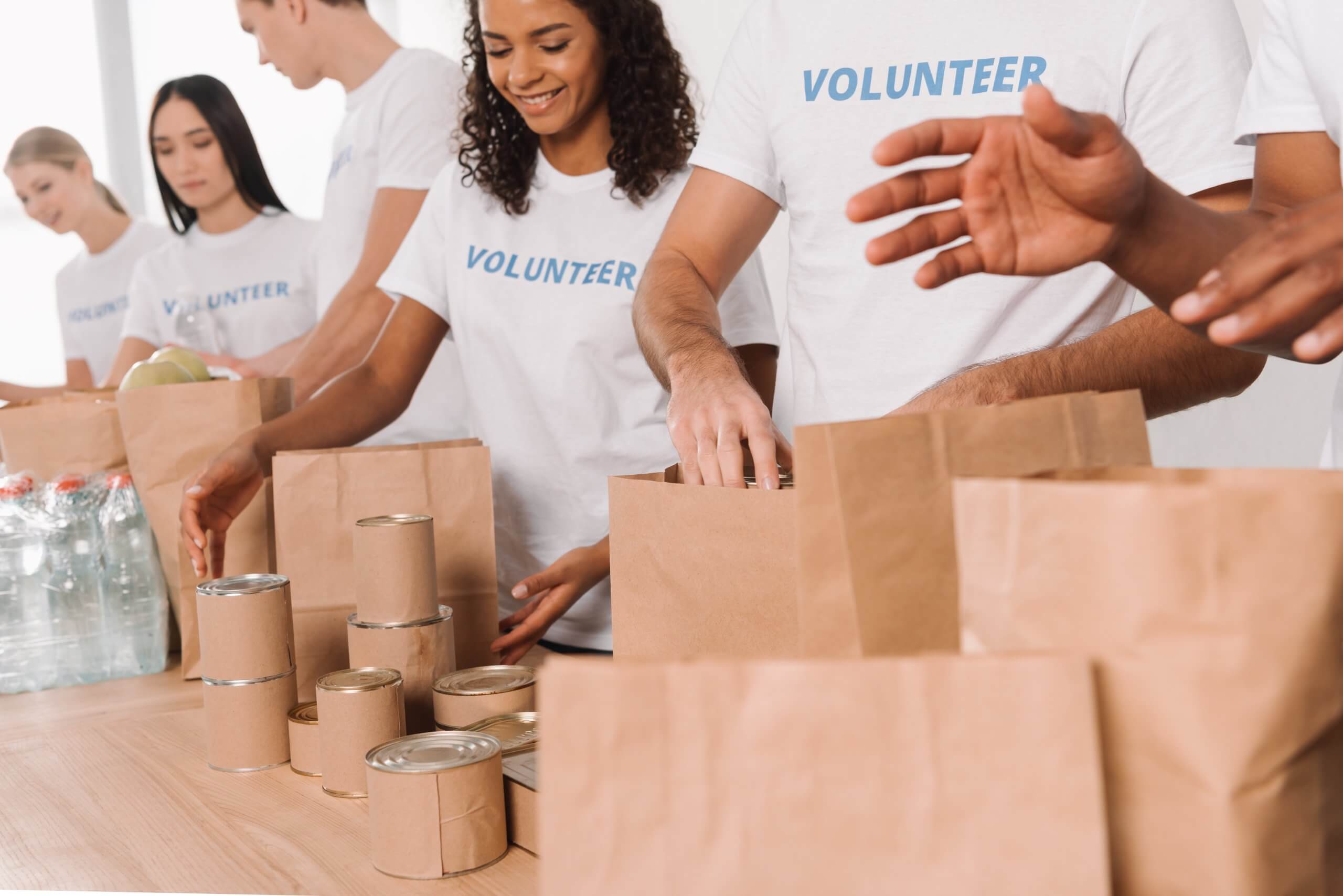 cropped shot of volunteers putting food and drinks into paper bags for charity