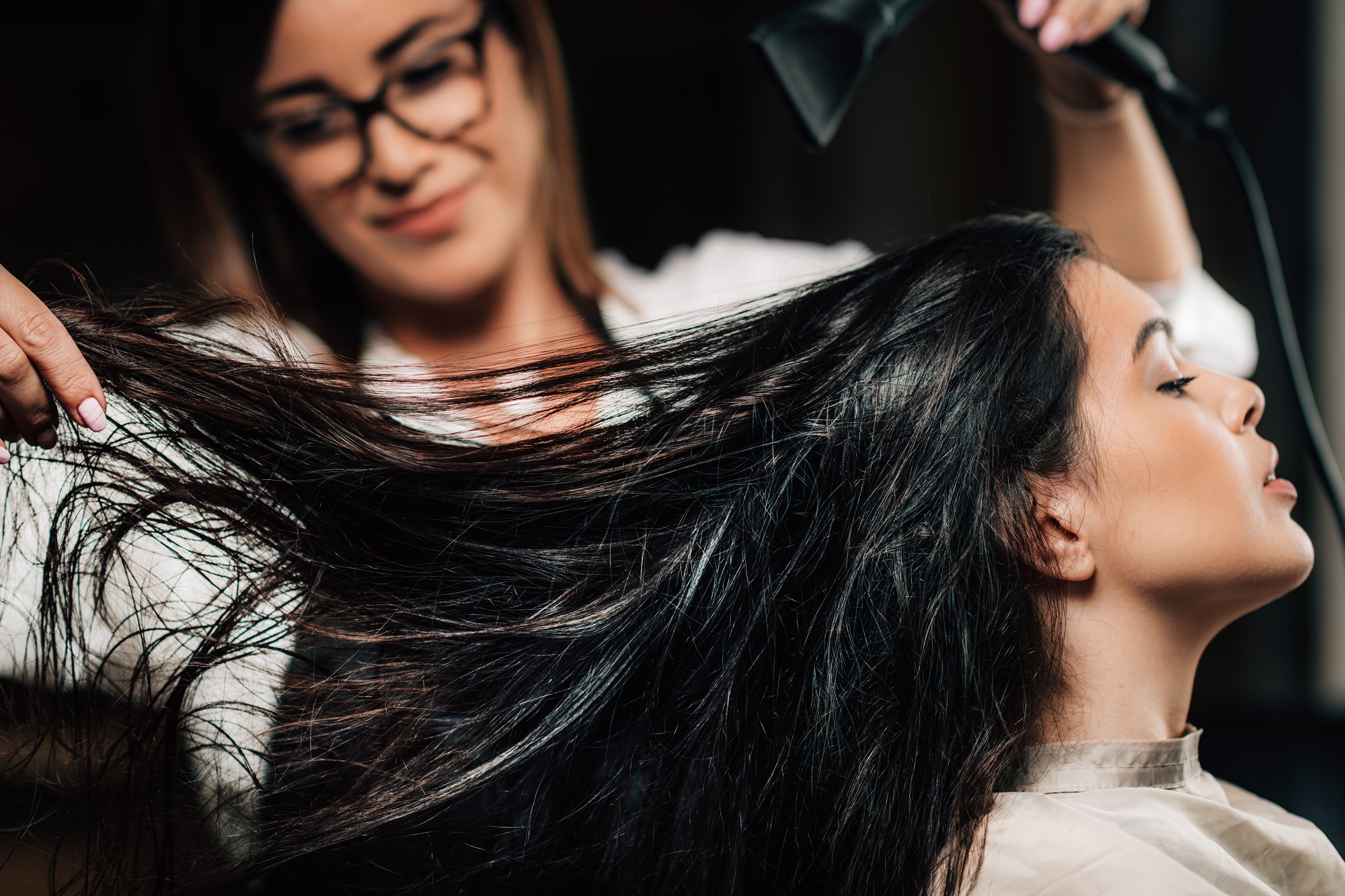 Hairdresser drying woman’s long black hair with hairdryer