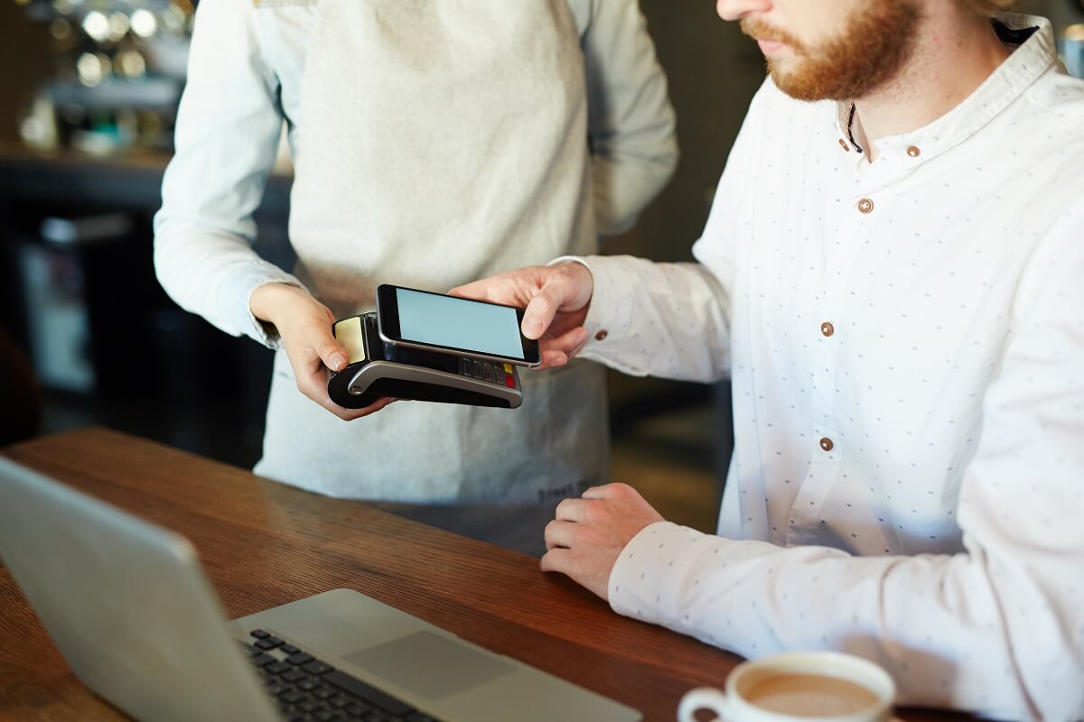 young man paying for his contactless order through nfc system in his smartphone in cafe