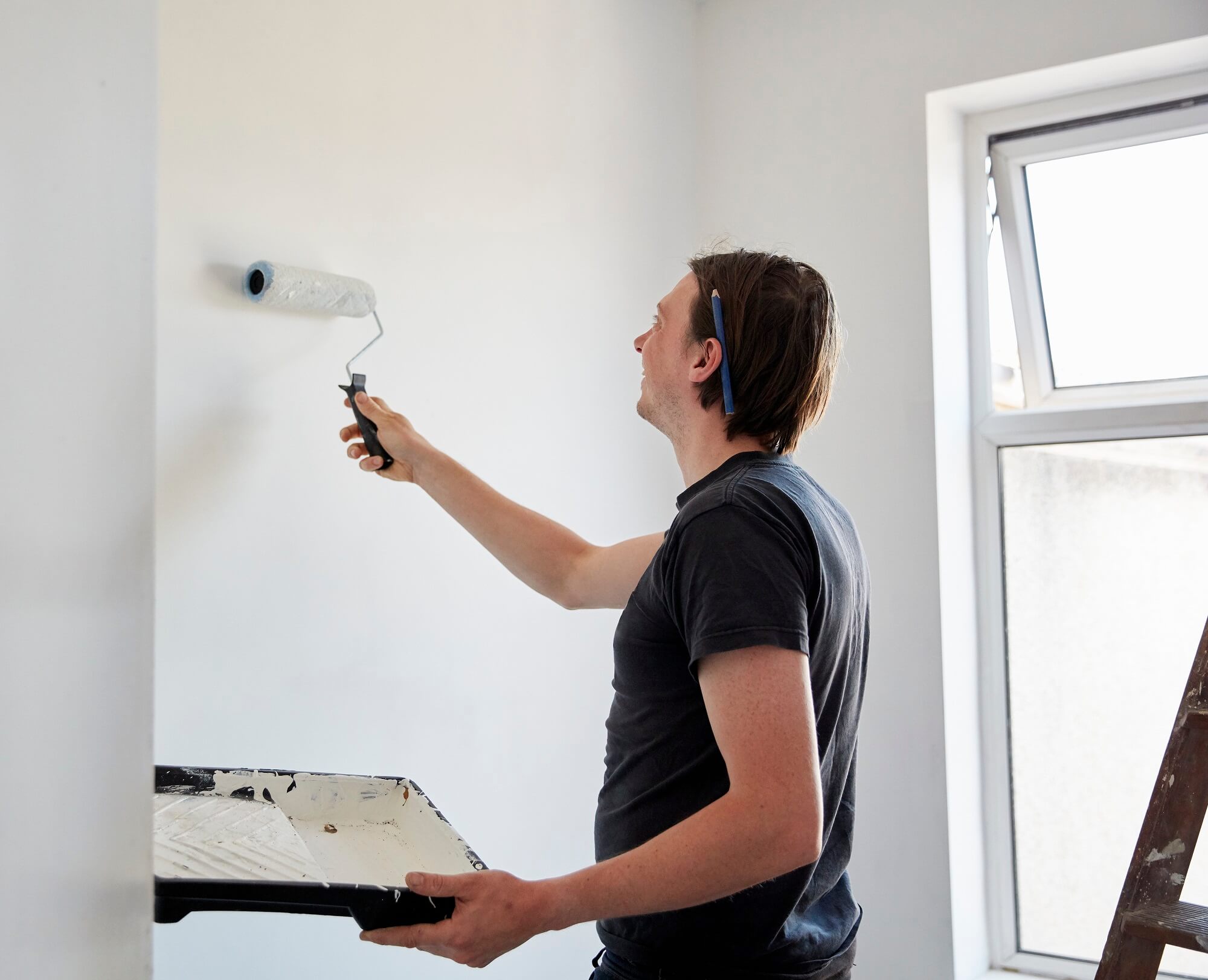 A painter using a paint roller and holding a paint tray, decorating a room.